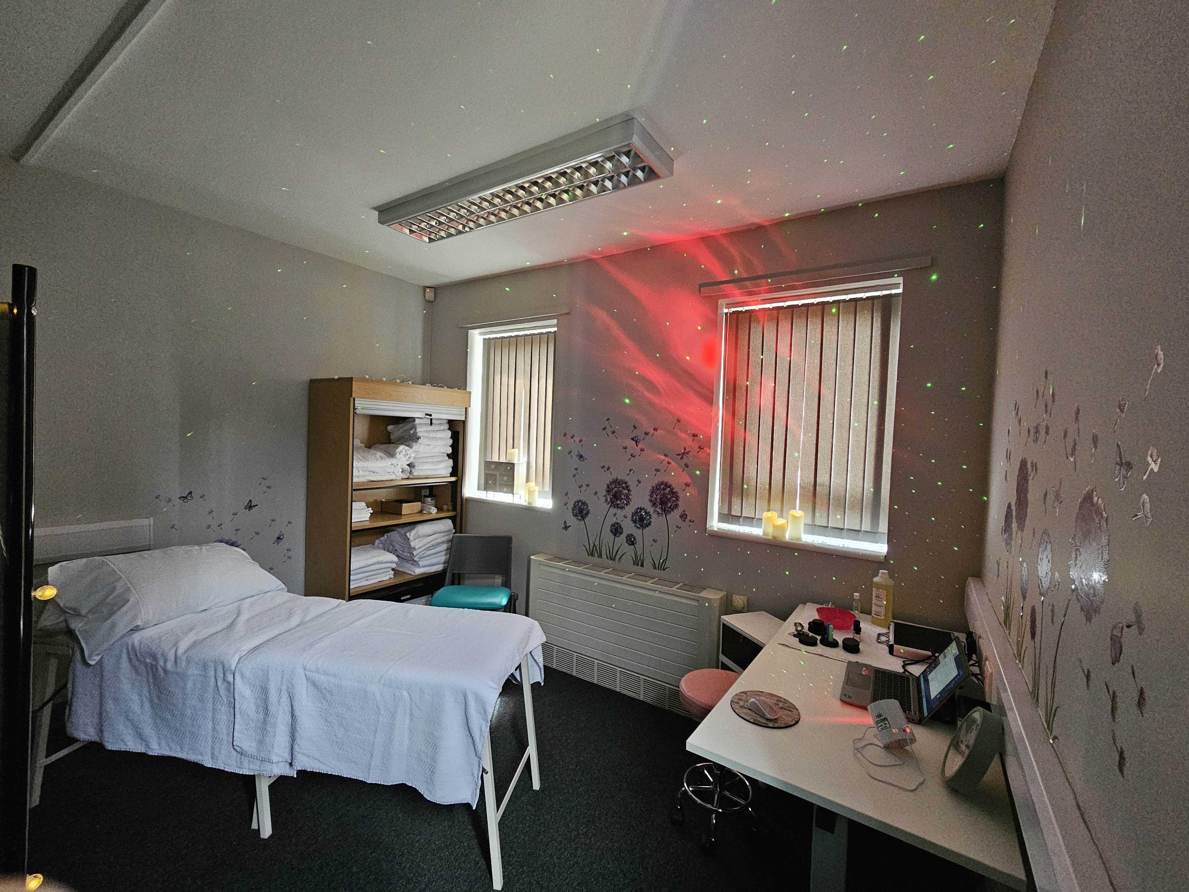 Picture of aromatherapy room. Includes a bed, shelves with towels on, red and green mood lighting and aromatherapy oils